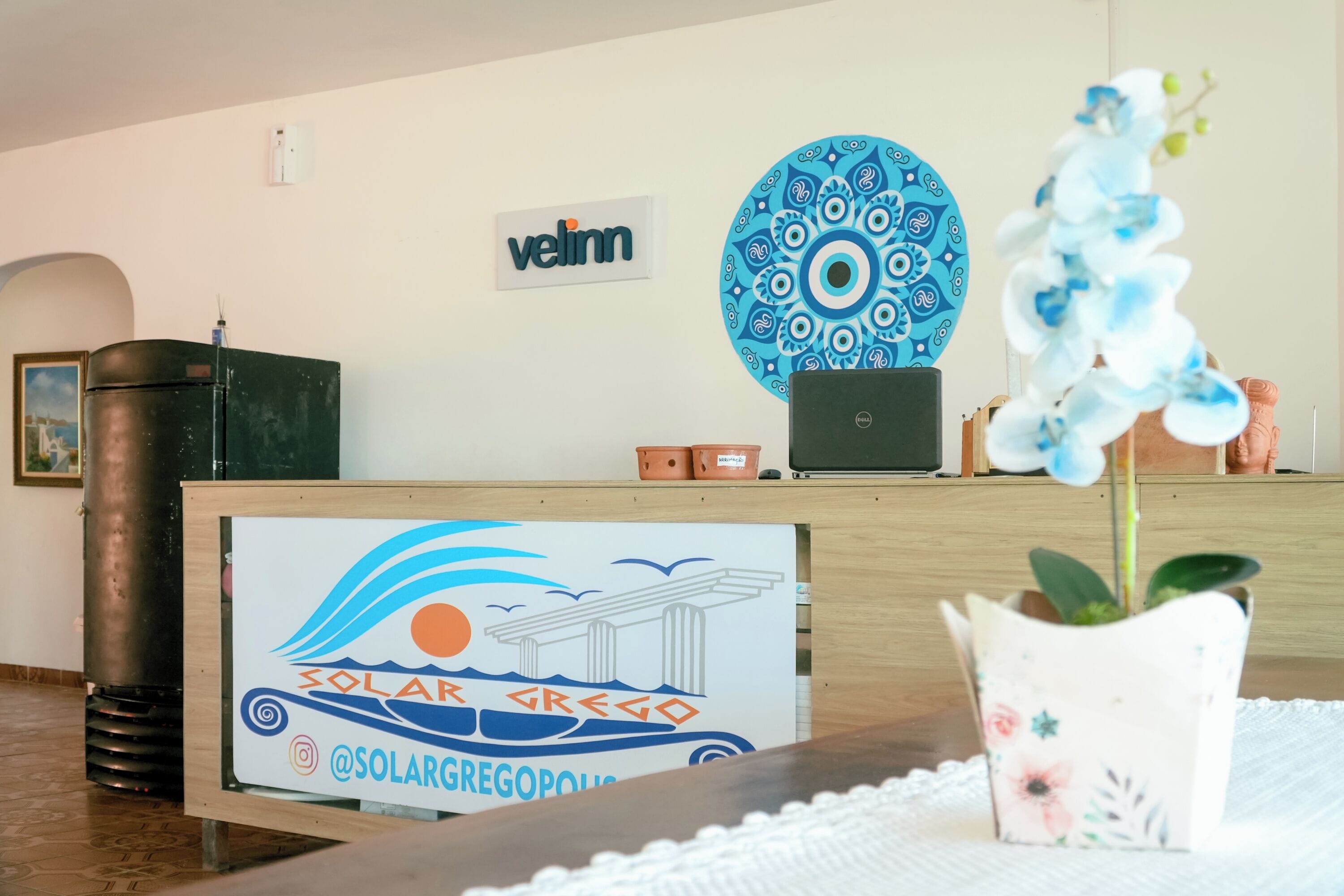Een receptiebalie met een bordje met de naam Solar Gregopolis, een laptop, een decoratief bord en een potorkidee.