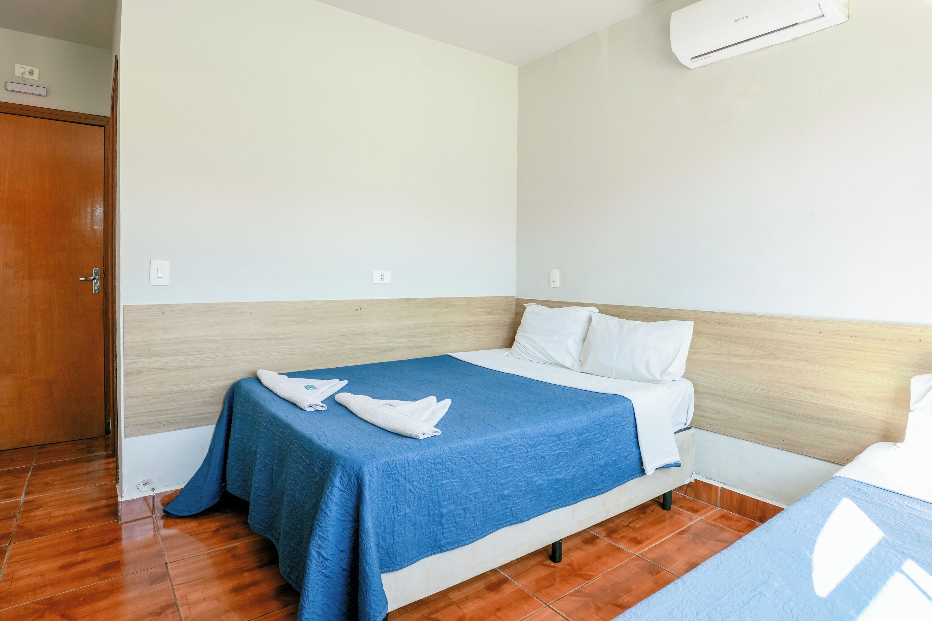 Habitació d'hotel amb un capçal de llit de fusta, un llit amb edredó blau, almoinos blancs i una mantella blanca doblegada al llit.