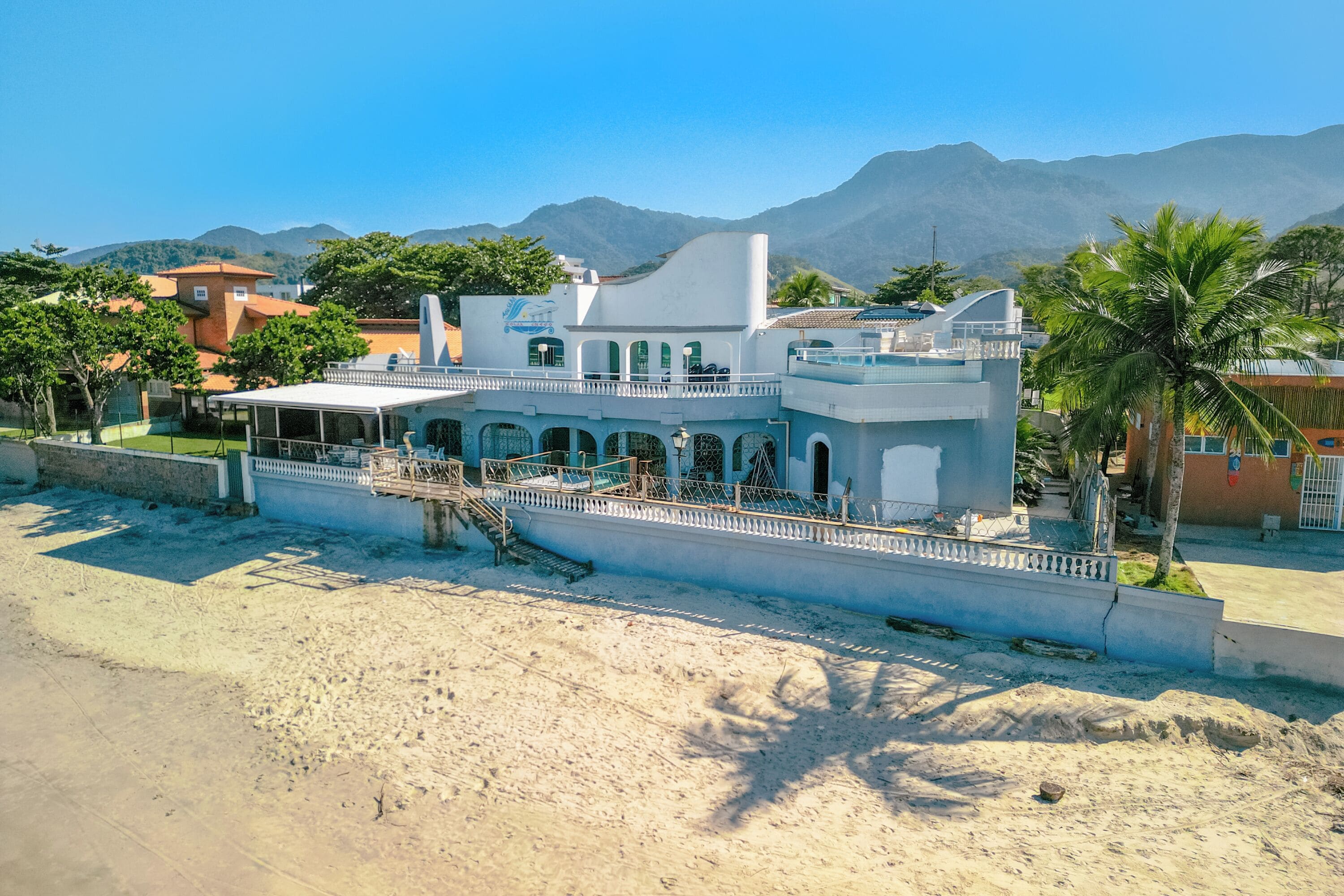 A beachfront property with a white building, a covered patio, and a view of mountains.