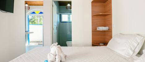 A bedroom with a bed, a wooden shelf, and a television mounted on the wall.
