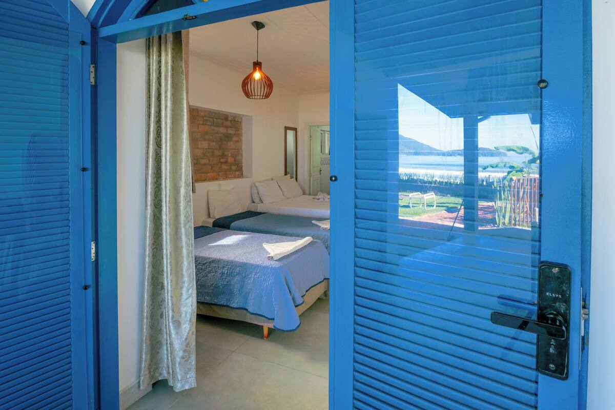Une chambre avec deux lits, une vue sur l’extérieur et une porte bleue.