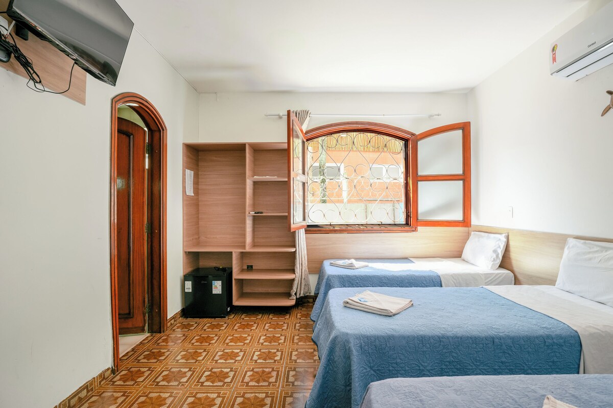 A hotel room with two beds, a wardrobe, a window with bars, and a television mounted on the wall.