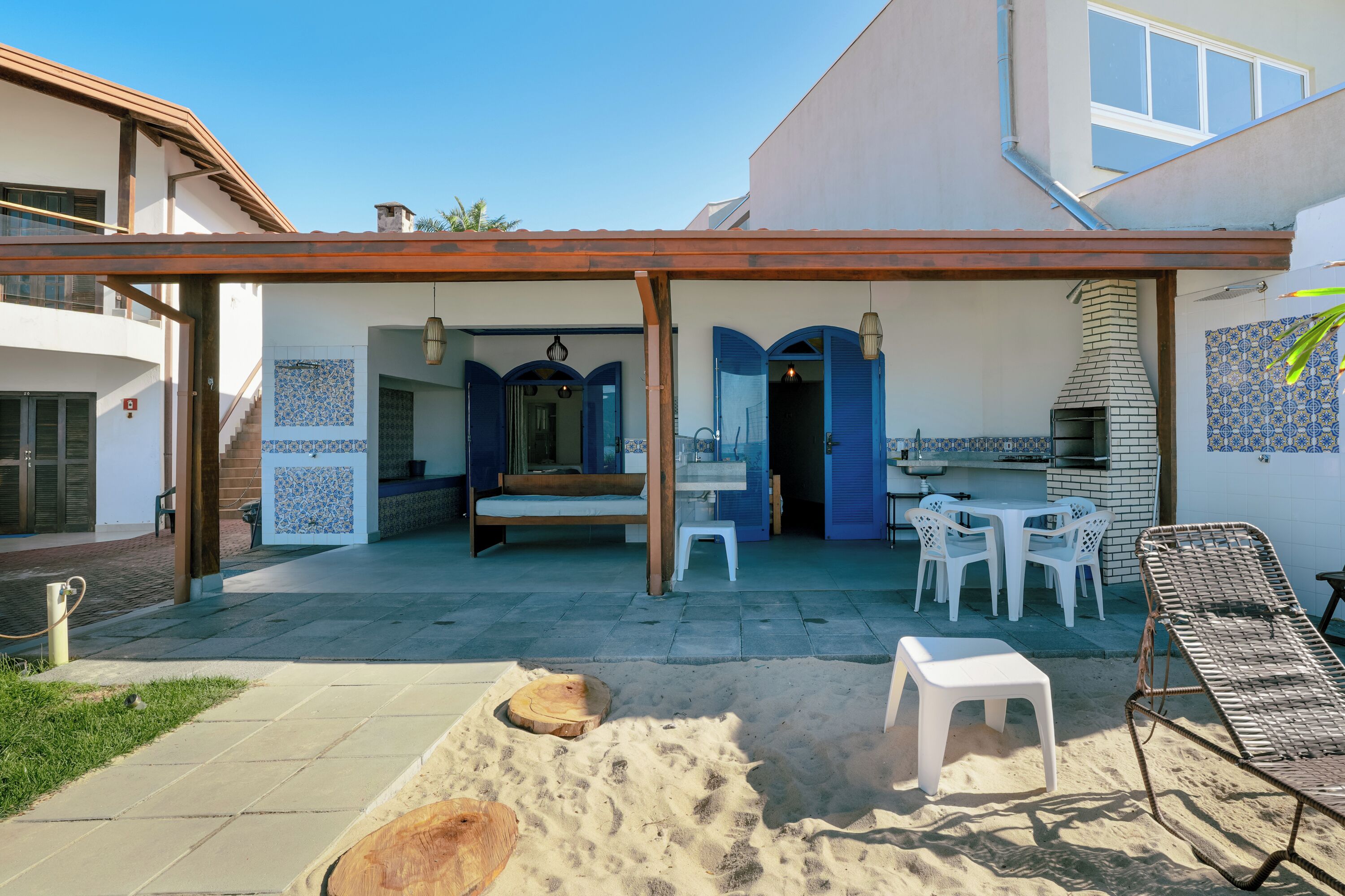 An outdoor patio with a wooden pergola, white plastic chairs, a small table, and a grill area.
