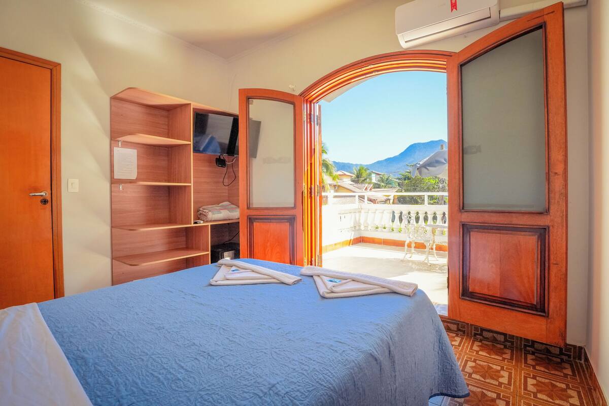 Une chambre d’hôtel avec un lit, une armoire en bois, une télévision et un balcon offrant une vue sur la montagne.