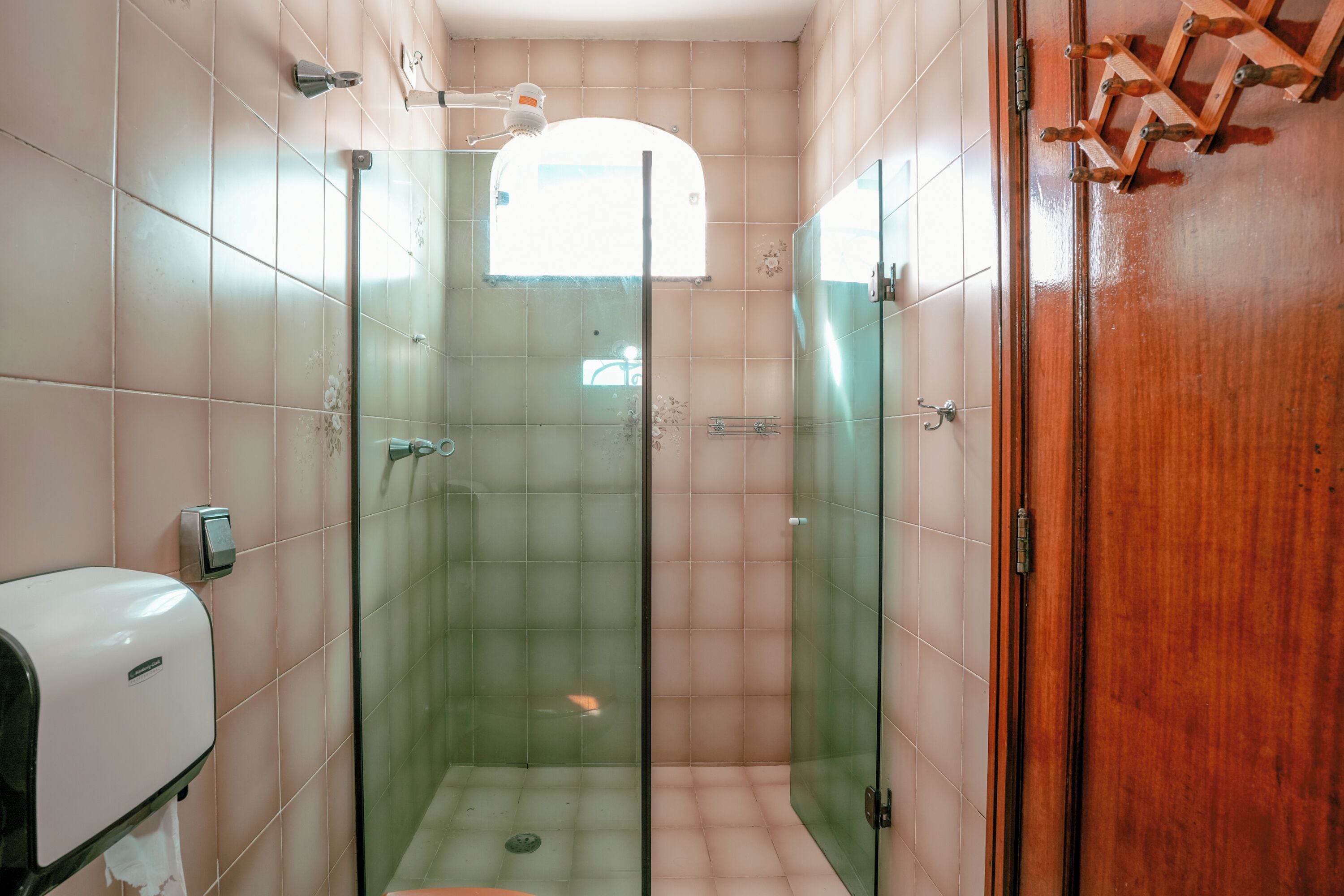 A glass-enclosed shower stall with a tiled wall, a wooden door, and a hand dryer.