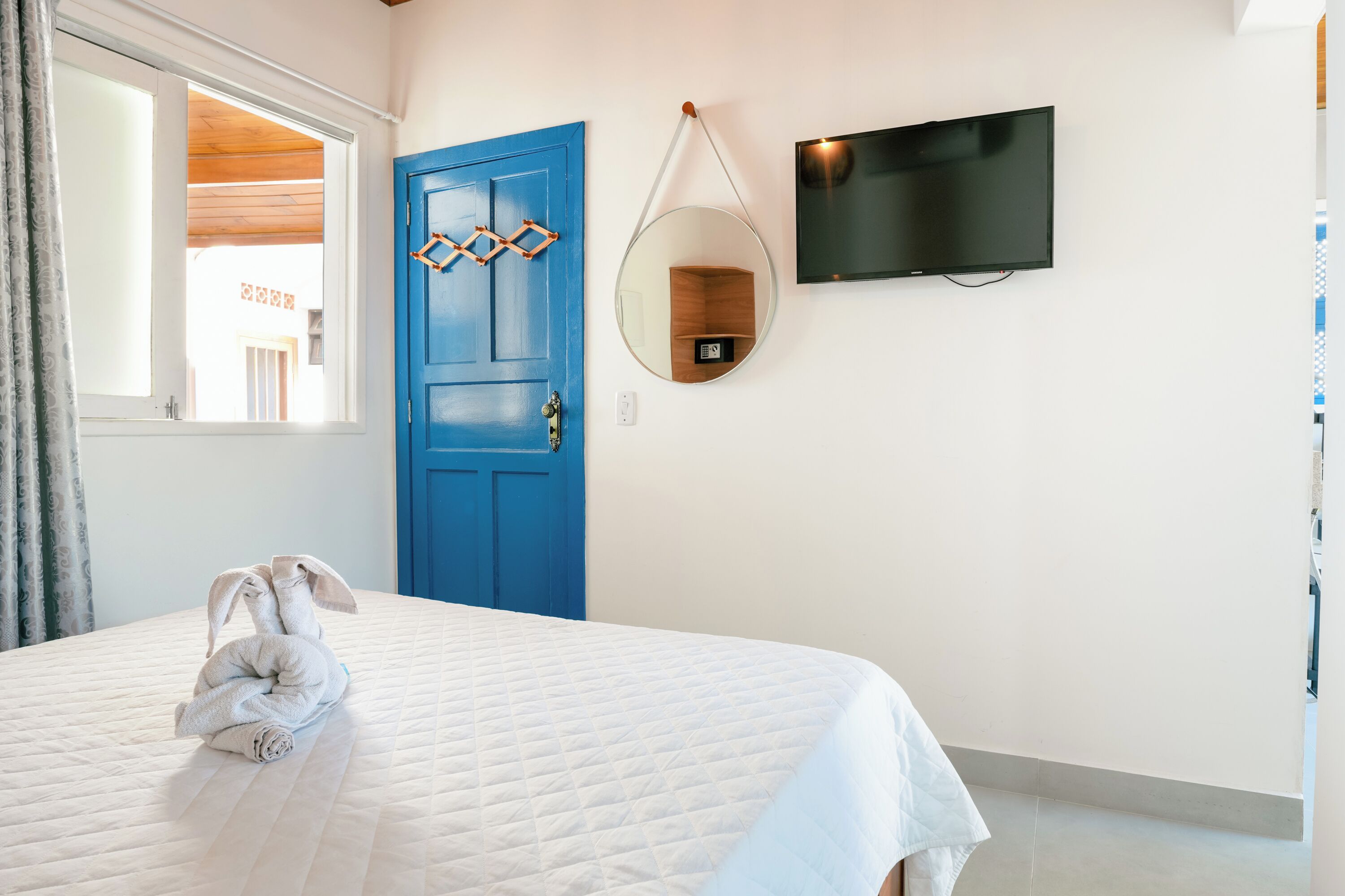 A hotel room with a bed, a blue door, a TV, and a mirror.