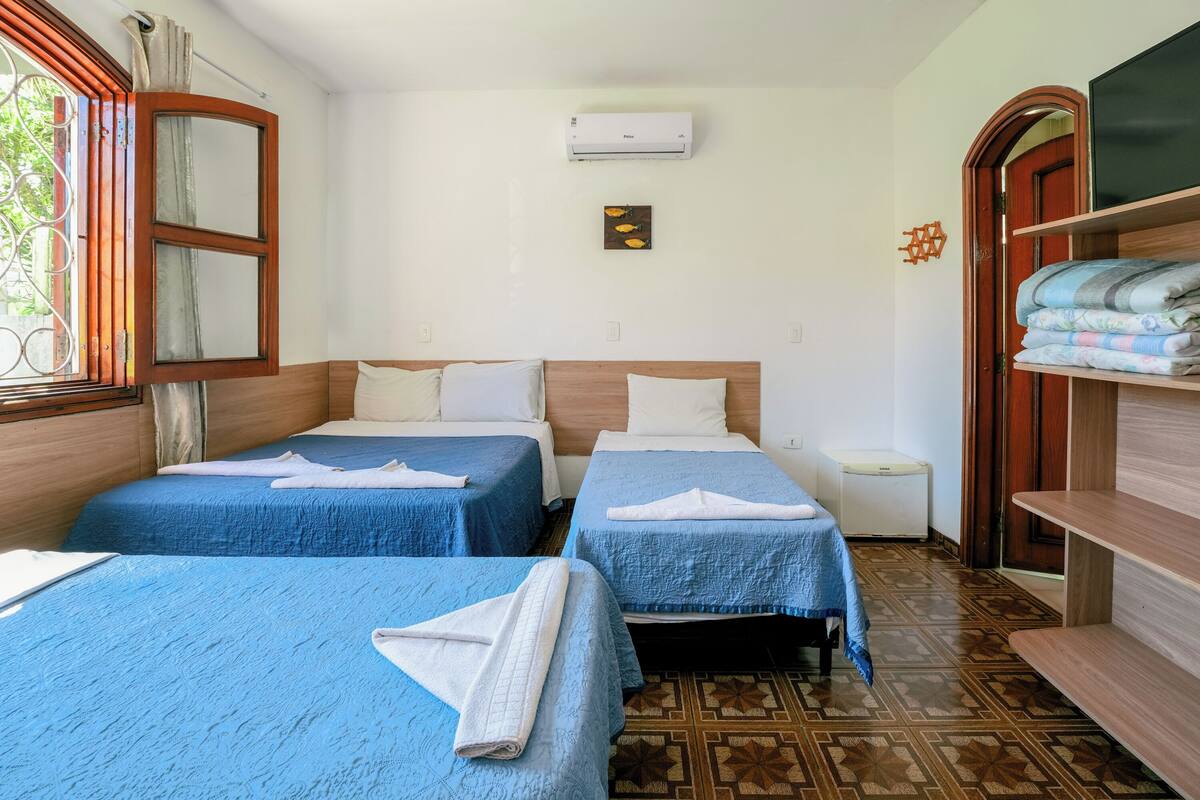 Une chambre d’hôtel avec deux lits, une armoire en bois, une petite table et un climatiseur fixé au mur.