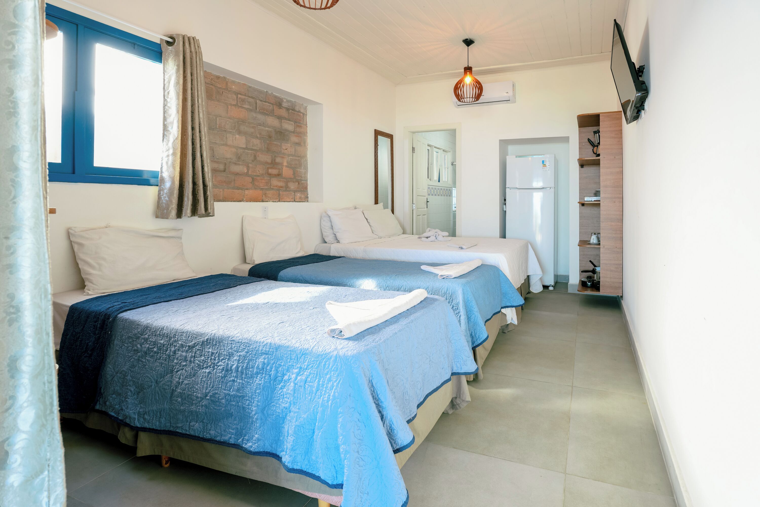 A hotel room with two beds, a brick accent wall, a flat-screen TV, and a kitchenette.