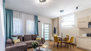 Una sala moderna con un sofá, una mesa de comedor y sillas, un área de cocina y un amplio ventanal con cortinas.