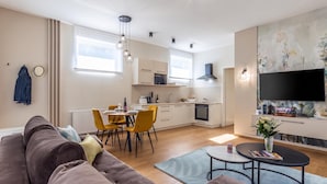 Una sala moderna con sofá, mesa de comedor y sillas, una cocina con electrodomésticos y un televisor montado en la pared.