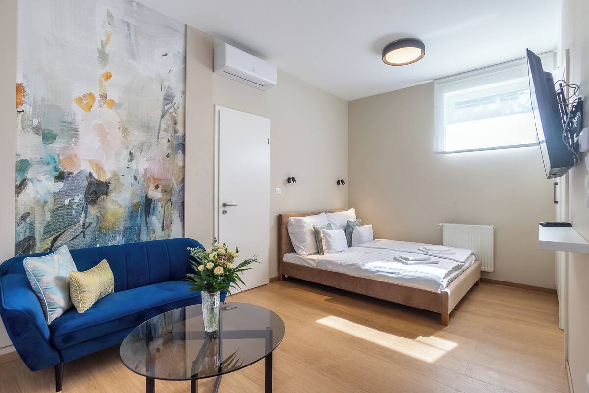 Una habitación moderna con sofá azul, cama, una mesita de centro de vidrio y un cuadro abstracto grande en la pared.