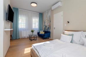 Ein Hotelzimmer mit Bett, Fernseher, Schreibtisch, Stuhl und einem Fenster mit Vorhängen.