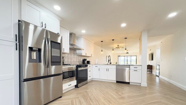 A modern kitchen with stainless steel appliances, white cabinetry, and a herringbone wood floor.