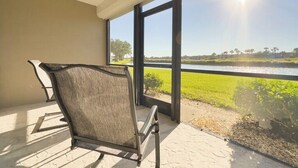 A balcony with a chair, large windows, and a view of a water body and greenery.