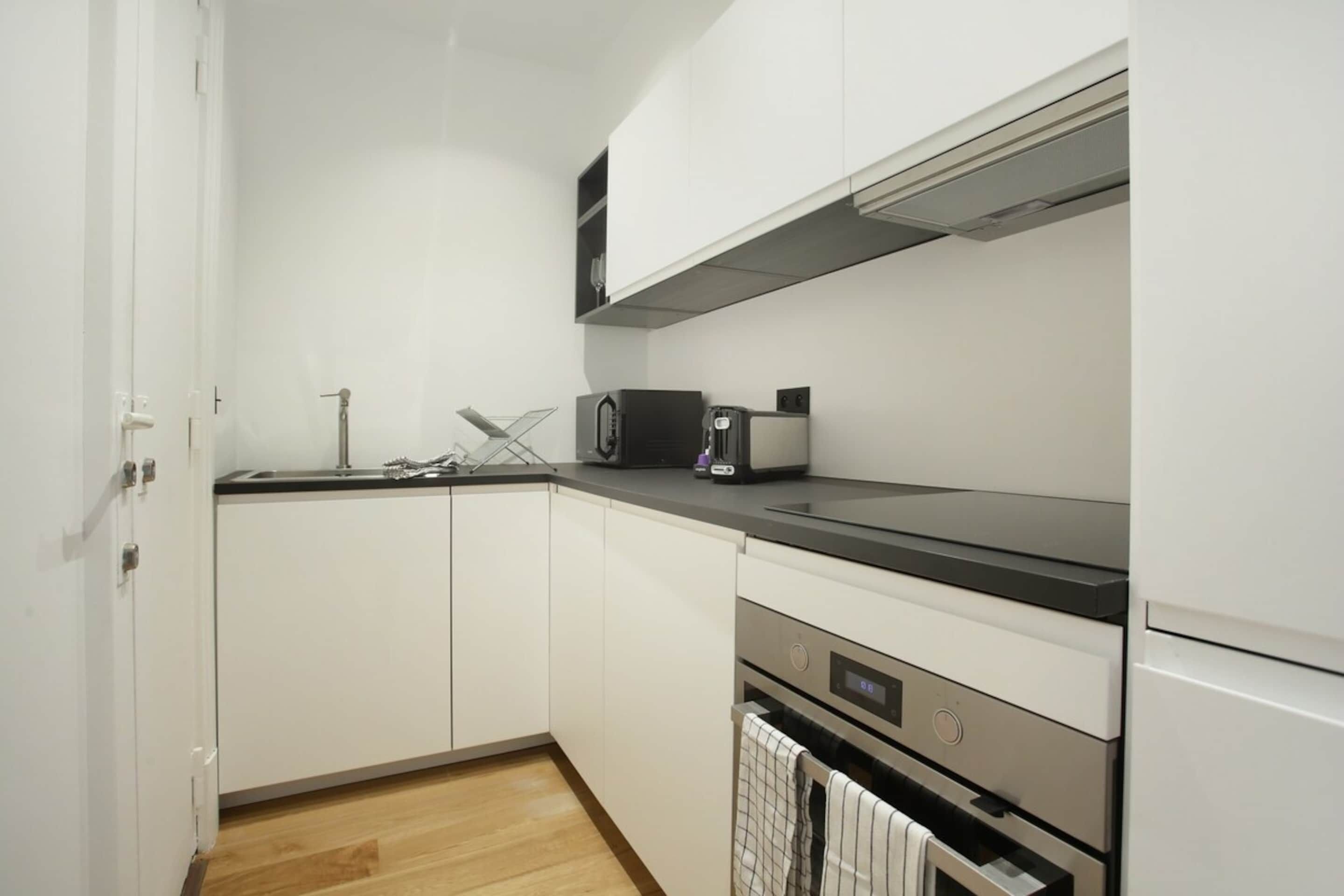 A kitchen with white cabinets, a black countertop, a microwave, a toaster, and a dishwasher.