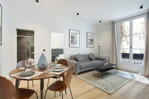 A modern living room with a dining area, a grey sofa, and a coffee table. - Elegant Apartment at the Palais Royal Opera (Paris)