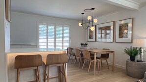 Een moderne keuken met een centraal eiland, barstoelen, een eettafel met stoelen, hanglampen en kunstwerken in lijsten aan de wanden.