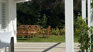 Een overdekt buitengebied met een houten terras, een barbecue en een zithoek.