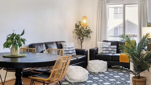 Ett modernt vardagsrum med ett matbord, en svart lädersoffa och vita sittpallar.