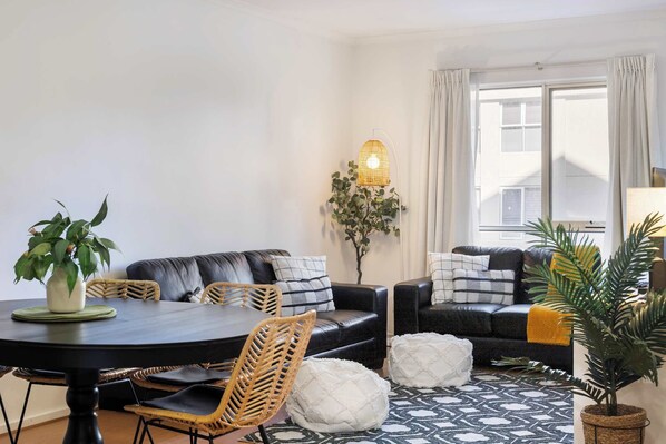 Un salon moderne avec une table à manger, un canapé en cuir noir et des poufs blancs.