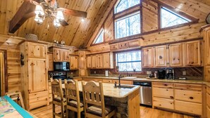 A wooden cabin interior with a kitchen area featuring wooden cabinets, a central island with bar stools, a built-in microwave, and a dishwasher. - Leaping Lizard Lodge | Sleeps 16 | 4 Beds | 3.5 Baths (Broken Bow)