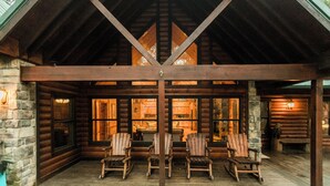 A log cabin with a covered porch, stone walls, and wooden furniture. - Leaping Lizard Lodge | Sleeps 16 | 4 Beds | 3.5 Baths (Broken Bow)