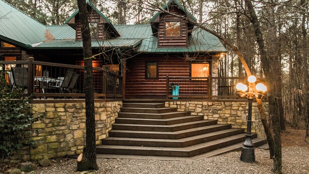 A log cabin with a stone staircase leading to the entrance, surrounded by trees. - Leaping Lizard Lodge | Sleeps 16 | 4 Beds | 3.5 Baths (Broken Bow)