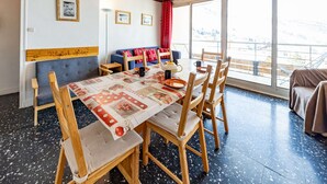 A dining area with a wooden table, chairs, and a view of a snowy landscape through large windows. - Spacious 8 pers. apartment at the foot of the slopes (Saint-François-Longchamp)