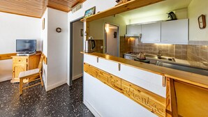 A compact kitchen with wooden cabinets, a built-in stove, and a small dining area with a chair. - Spacious 8 pers. apartment at the foot of the slopes (Saint-François-Longchamp)