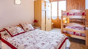 A cozy bedroom with a wooden bunk bed, a single bed with a quilt, a nightstand, a red lamp, and a wooden wardrobe. - Spacious 8 pers. apartment at the foot of the slopes (Saint-François-Longchamp)