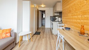 Een moderne keuken met houten kastjes, een eethoek met een tafel en stoelen, en een bank met oranje kussens.