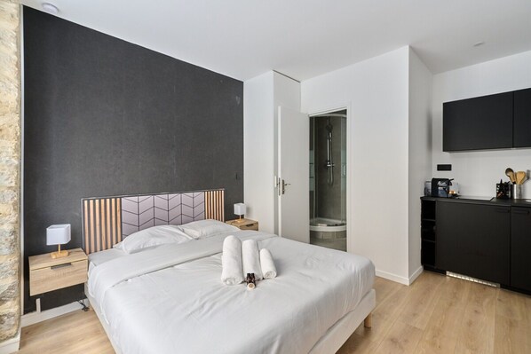 Moderni hotellihuone, jossa on suuri sänky, suihku, taulutelevisio ja pieni keittopiste.