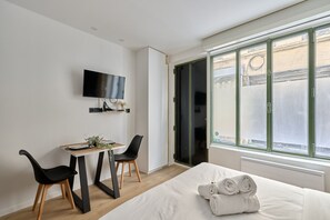 Hotellihuone, jossa on sänky, työpöytä ja kaksi tuolia, televisio sekä suuri ikkuna, josta on n äkymä ulos.