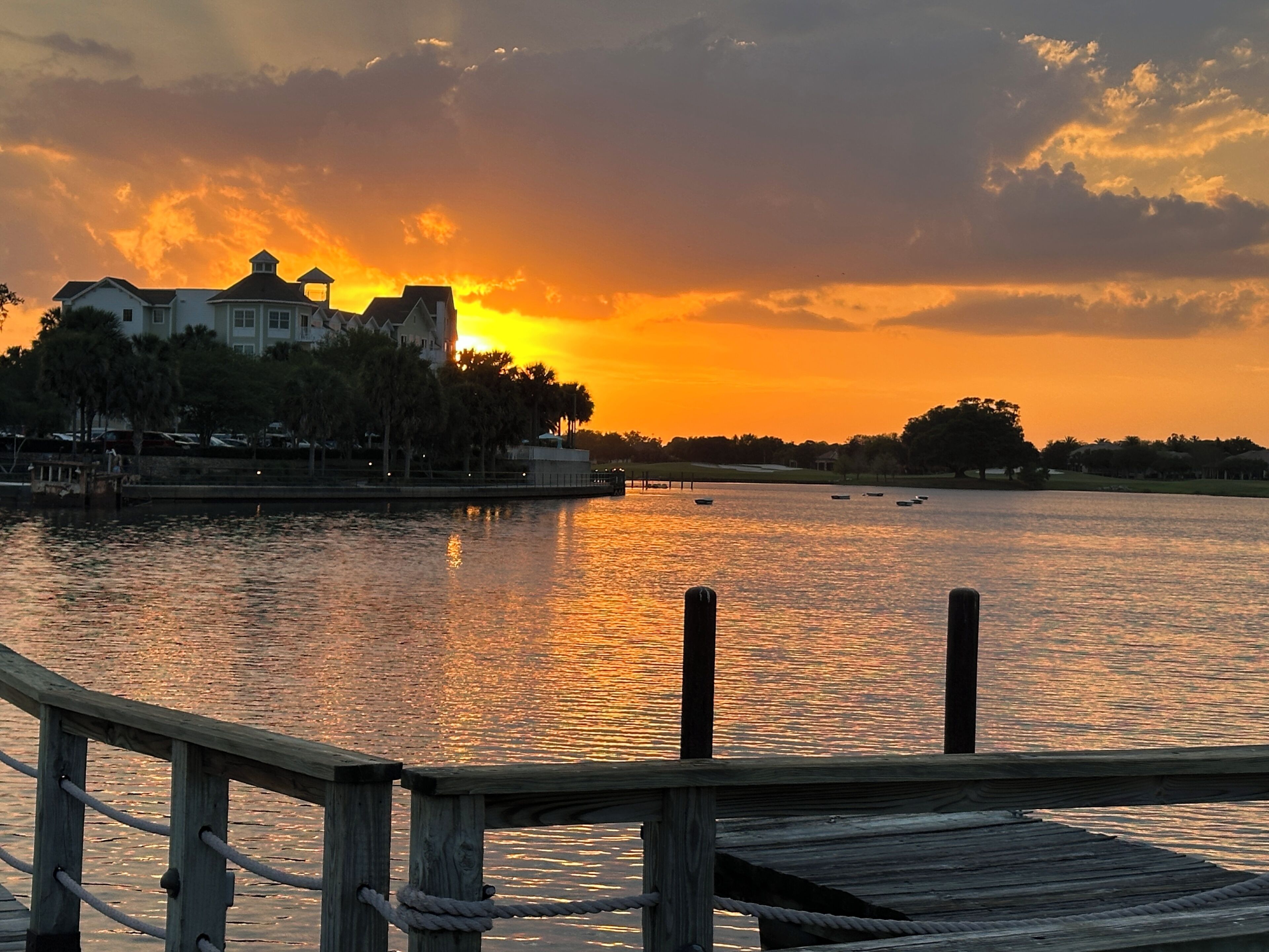 A waterfront view with a wooden dock, calm water, and a sunset in the background.