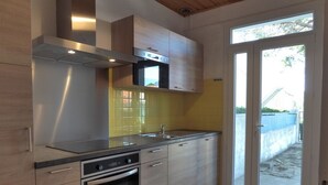 A modern kitchen with stainless steel appliances, wooden cabinets, and a large sliding glass door leading to an outdoor area. - 2-bedroom apartment near beach, private garden, pets allowed (Argelès-sur-Mer)