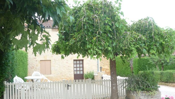 A stone building with a white picket fence, a small table and chairs, and a potted plant.