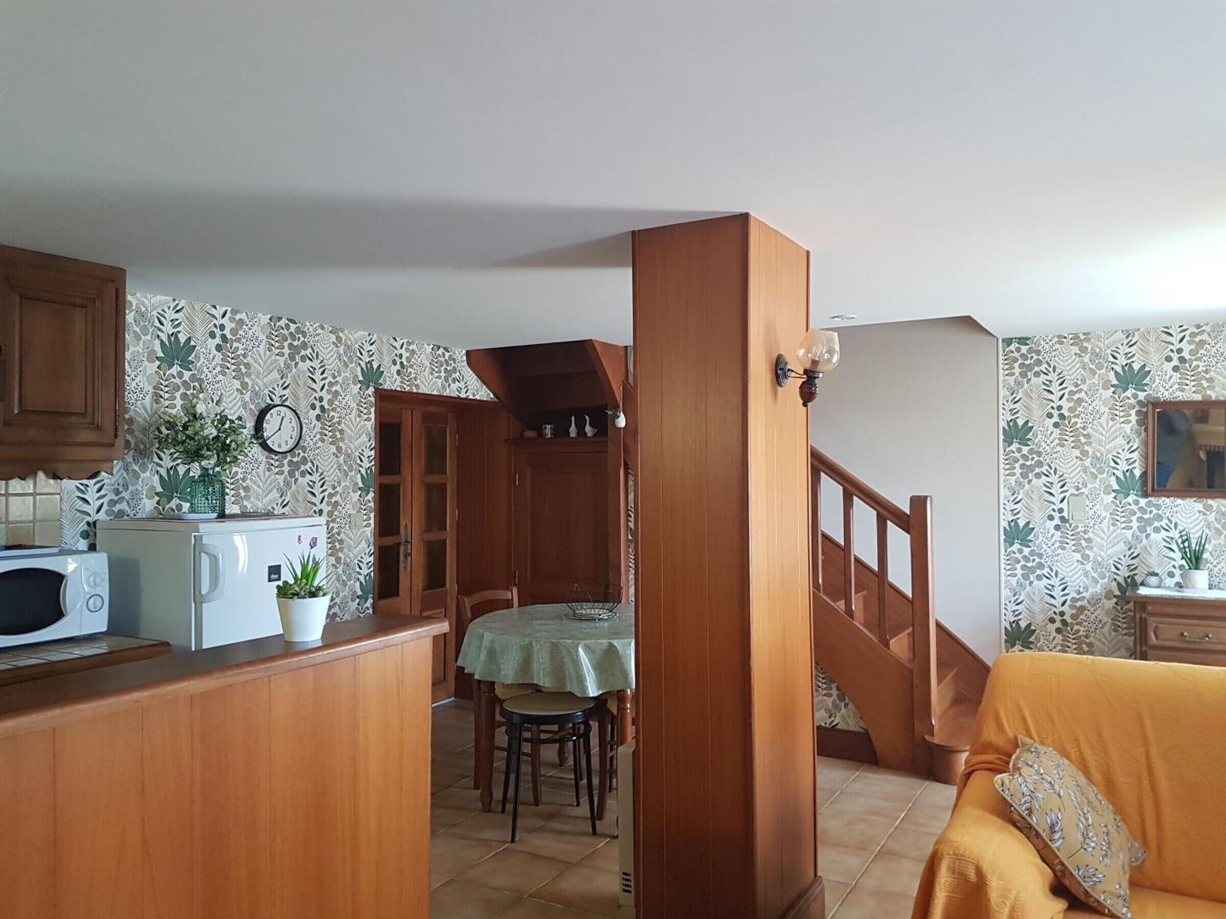 Una cocina con armarios de madera, microondas, una mesa de comedor con sillas y una escalera que lleva a otra habitación.