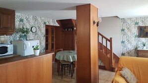 A kitchen with wooden cabinets, a microwave, a dining table with chairs, and a staircase leading to another room.