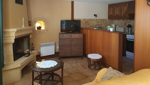 A compact living space with a fireplace, a television, a small kitchen area, and a cozy seating area with a sofa and two stools.