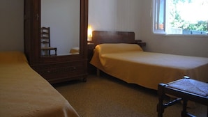 Habitación con dos camas individuales, un armario de madera, una silla y una ventana con vista a áreas verdes.