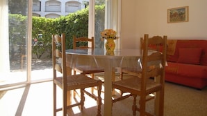 Un comedor con una mesa de vidrio y sillas de madera, un sofá rojo y un jarrón con flores.