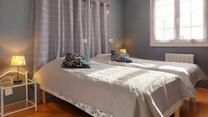 Un dormitorio con dos camas, una mesita de noche, una lámpara, una ventana con cortinas y una lámpara en el techo.