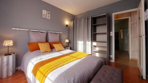 Un dormitorio con cama, mesitas de noche, armario y baño visible a través de una puerta abierta.