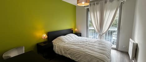 A bedroom with a bed, bedside lamps, a desk, and a window with curtains.