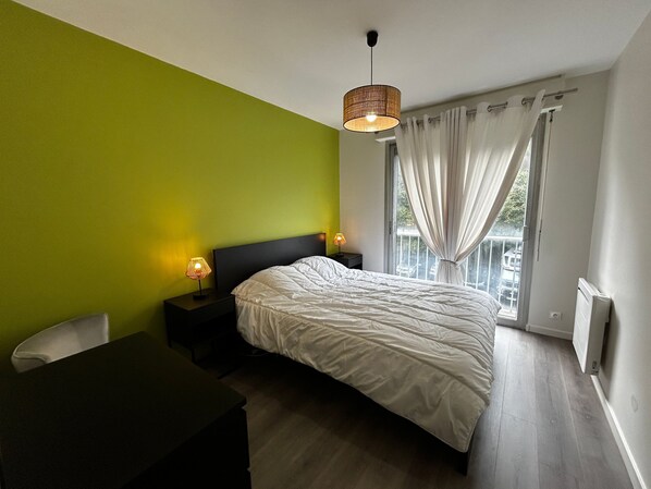A bedroom with a bed, bedside lamps, a desk, and a window with curtains.