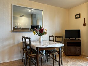 A dining area with a table, chairs, a vase with flowers, a television, and a cabinet.