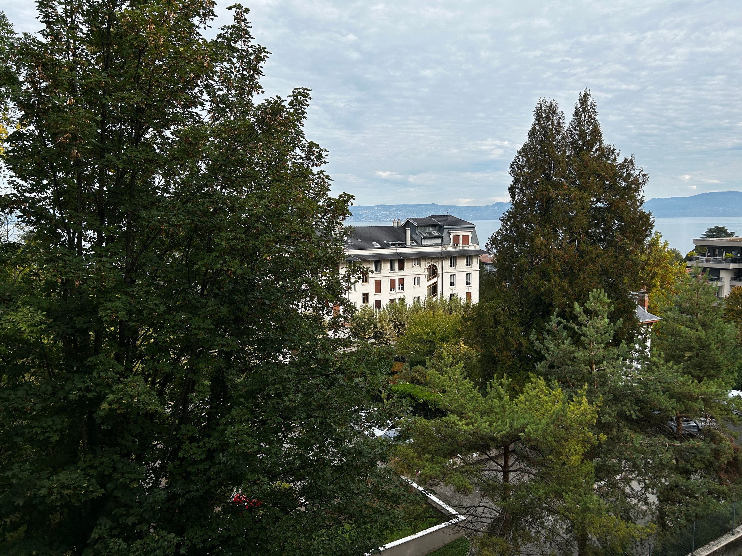 A large building with multiple windows and a balcony, surrounded by dense trees.