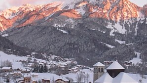 Un village de montagne aux maisons recouvertes de neige et à l’église imposante, dotée d’un clocher.