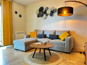 A living room with a grey sofa, yellow cushions, a coffee table, a wall art piece, and a floor lamp.
