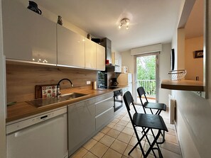 A modern kitchen with white cabinets, a wooden countertop, and a built-in dishwasher. There are two black chairs and a small table. - Spacious refurbished apartment with balcony and garage, near city center (Évian-les-Bains)